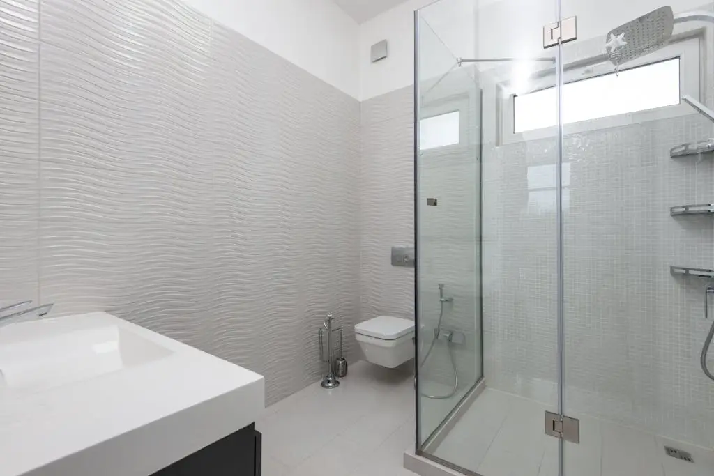 Shower room with glass walls against toilet bowl and washbasin above tiled floor in light house